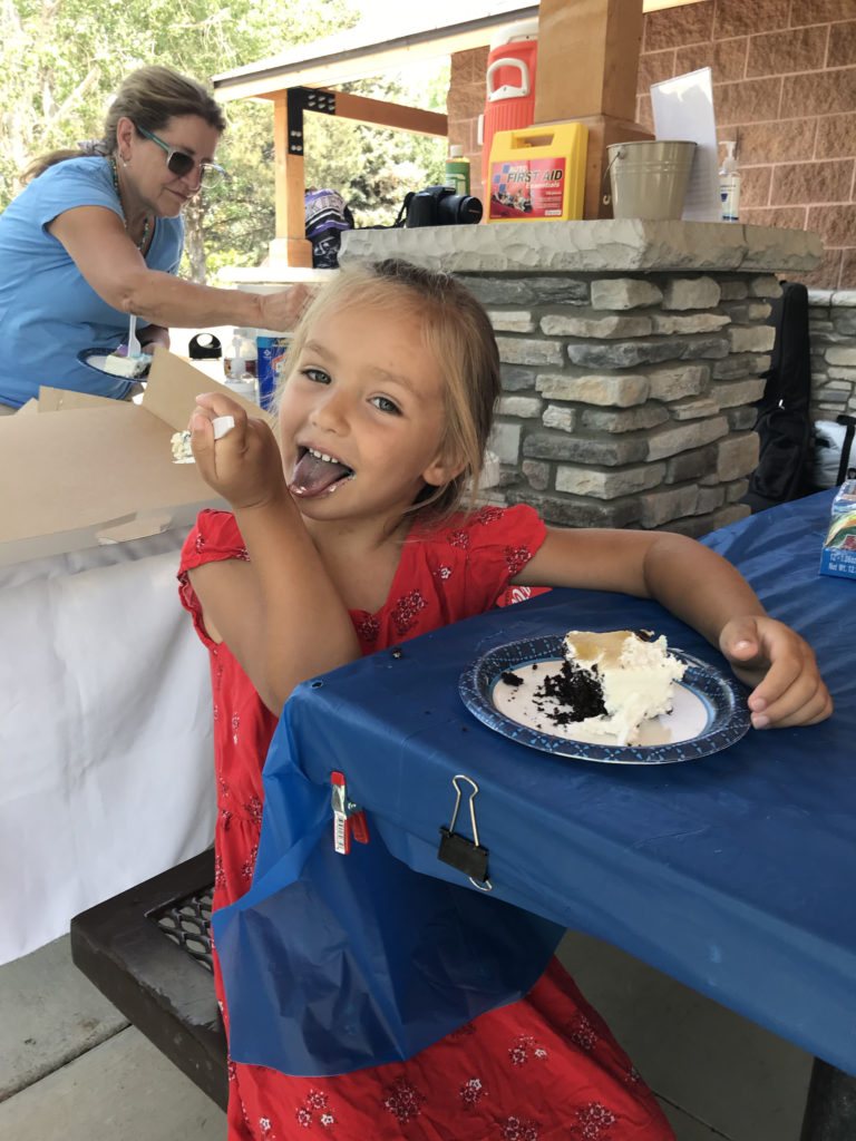 Child in red dress eating cake and licking her hand.