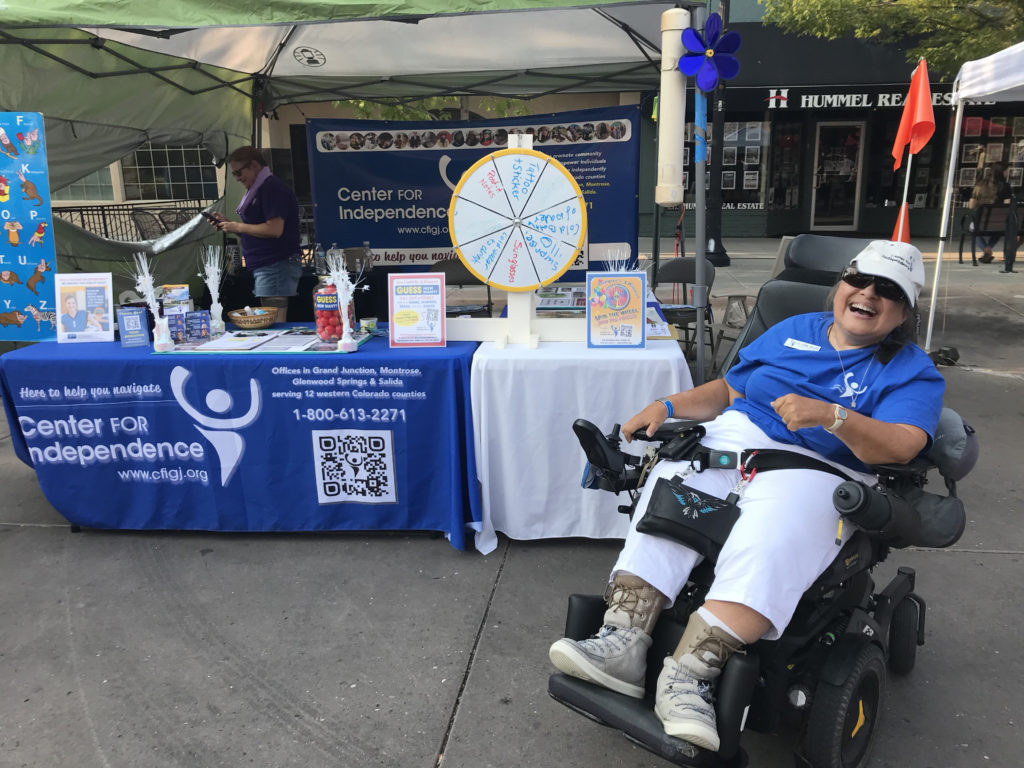 Lynn Jolley in her motorized wheelchair sits in front of the CFI booth at Grand Junction's Market on Main Farmers Market 