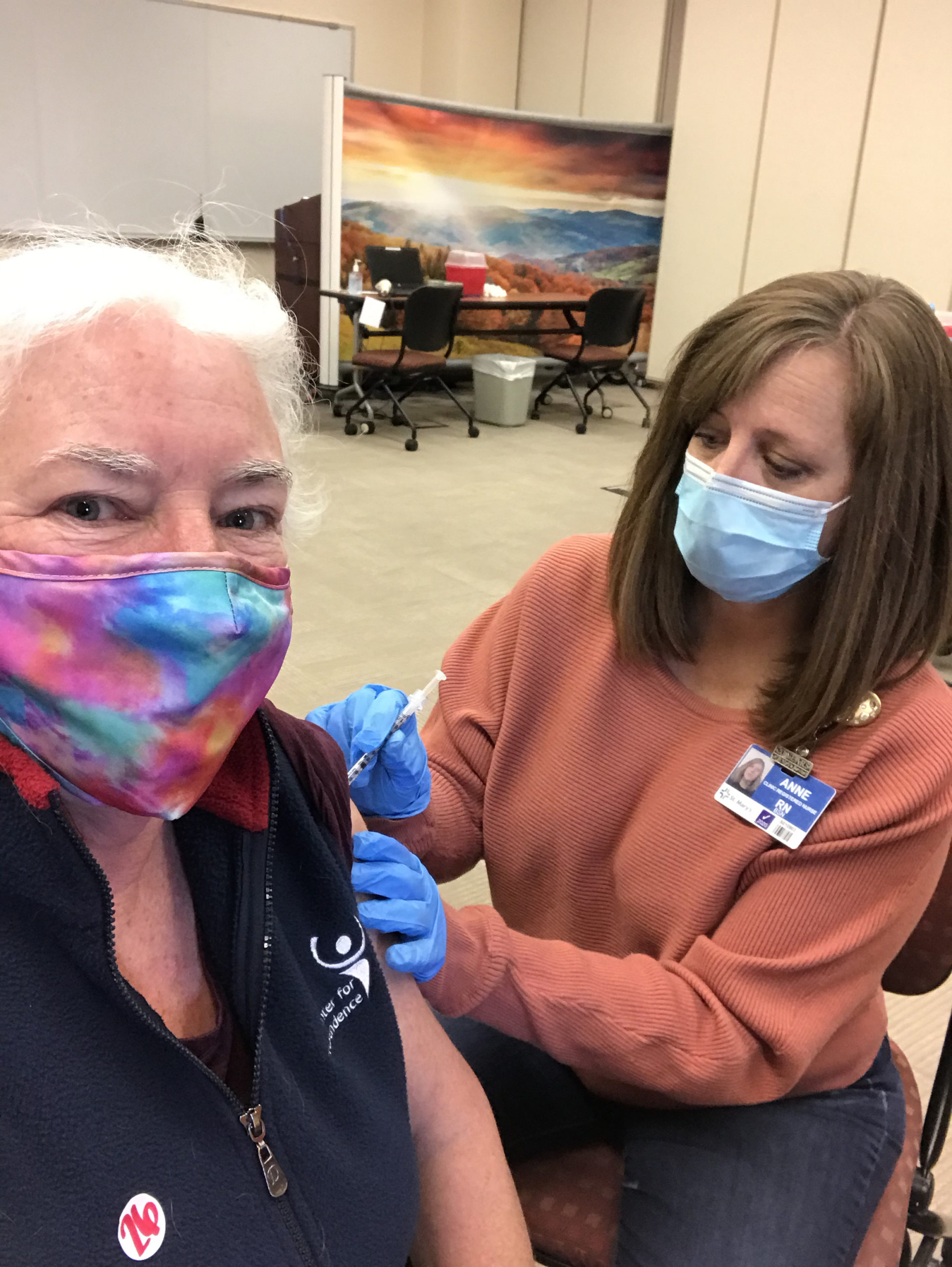 Woman with mask receives a vaccine from a nurse in a mask.