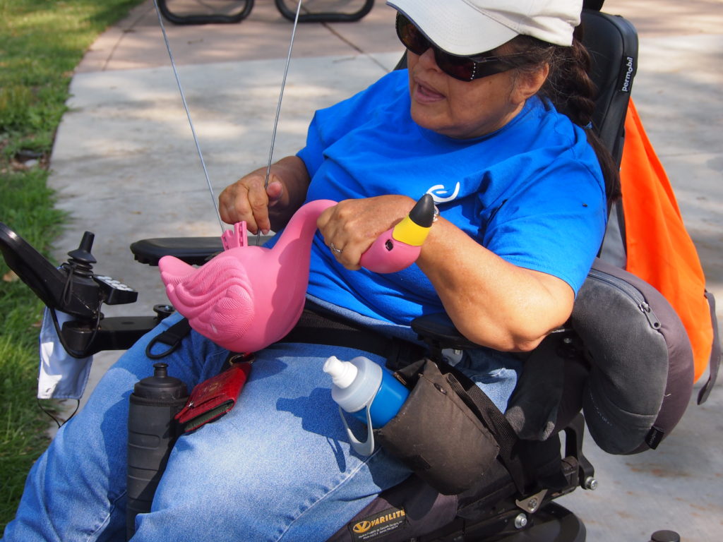 Woman in scooter chair puts legs on plastic flamingo.