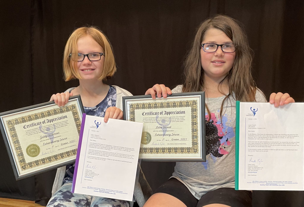 Two young girls sit together displaying certificates of recognition for their fundraising efforts on behalf of CFI.