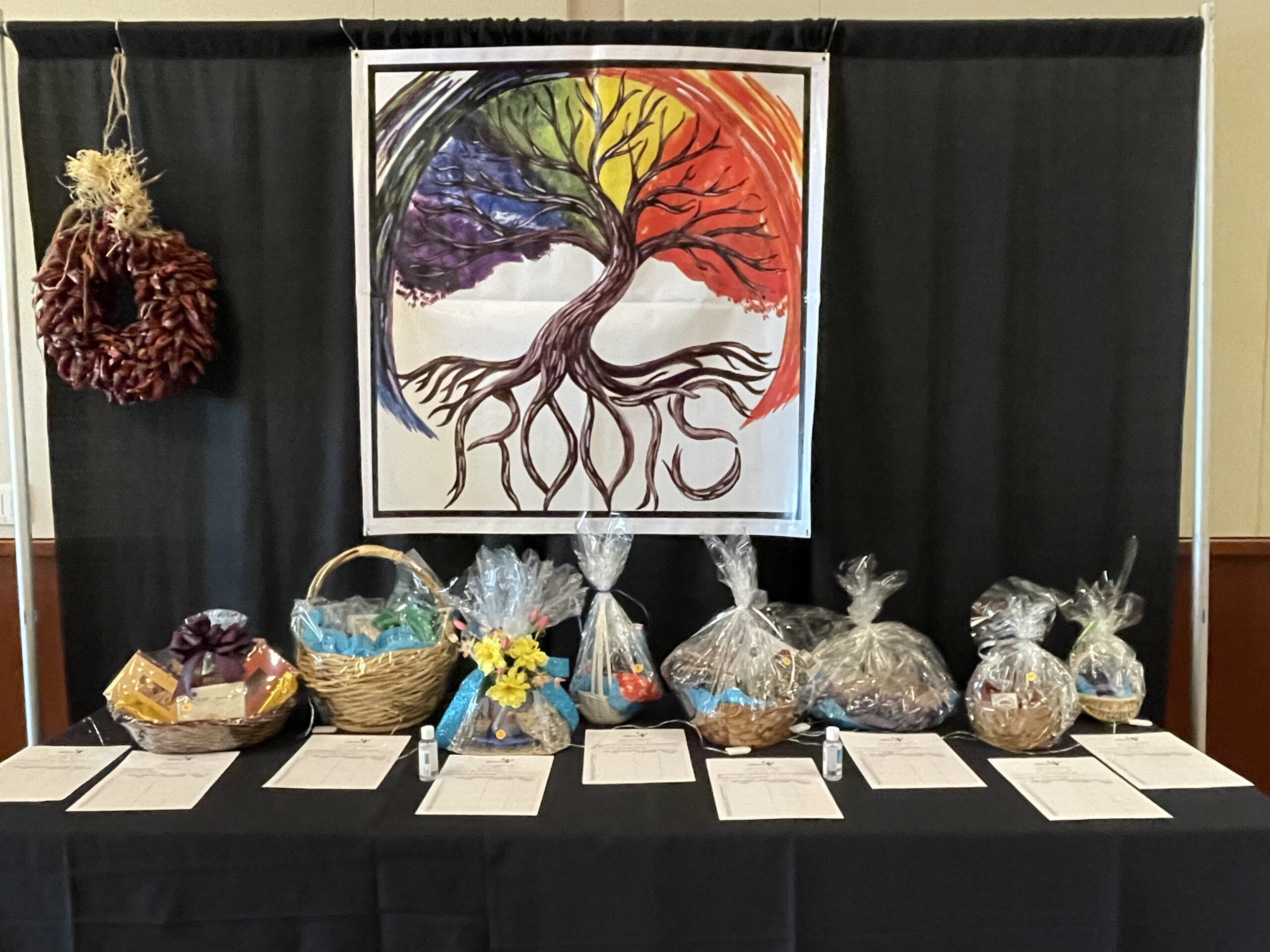 Silent auction baskets sit on a table in front of Roots banner, one of CFI's banner sponsors for the 40th Celebration event at CMU ballroom.