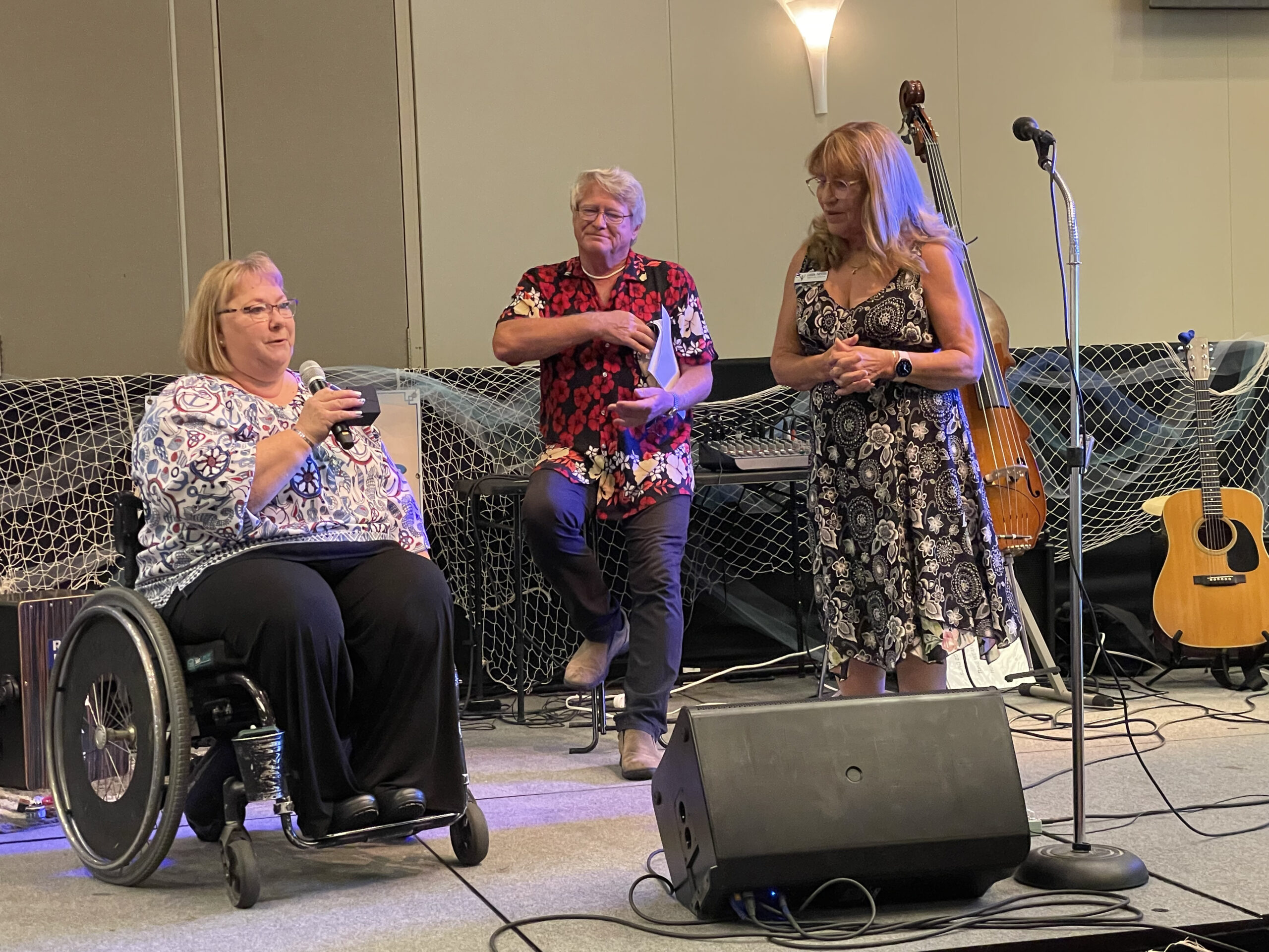 Board members Jennifer Shook and Greg Mueller present outgoing CEO Linda Taylor with a gift while standing on a stage with musical instruments behind them at the CMU ballroom.